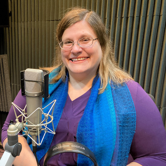 A smiling woman sits in front of a microphone.