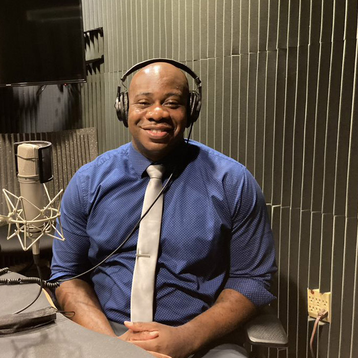 A smiling man in a shirt and tie is wearing headphones.
