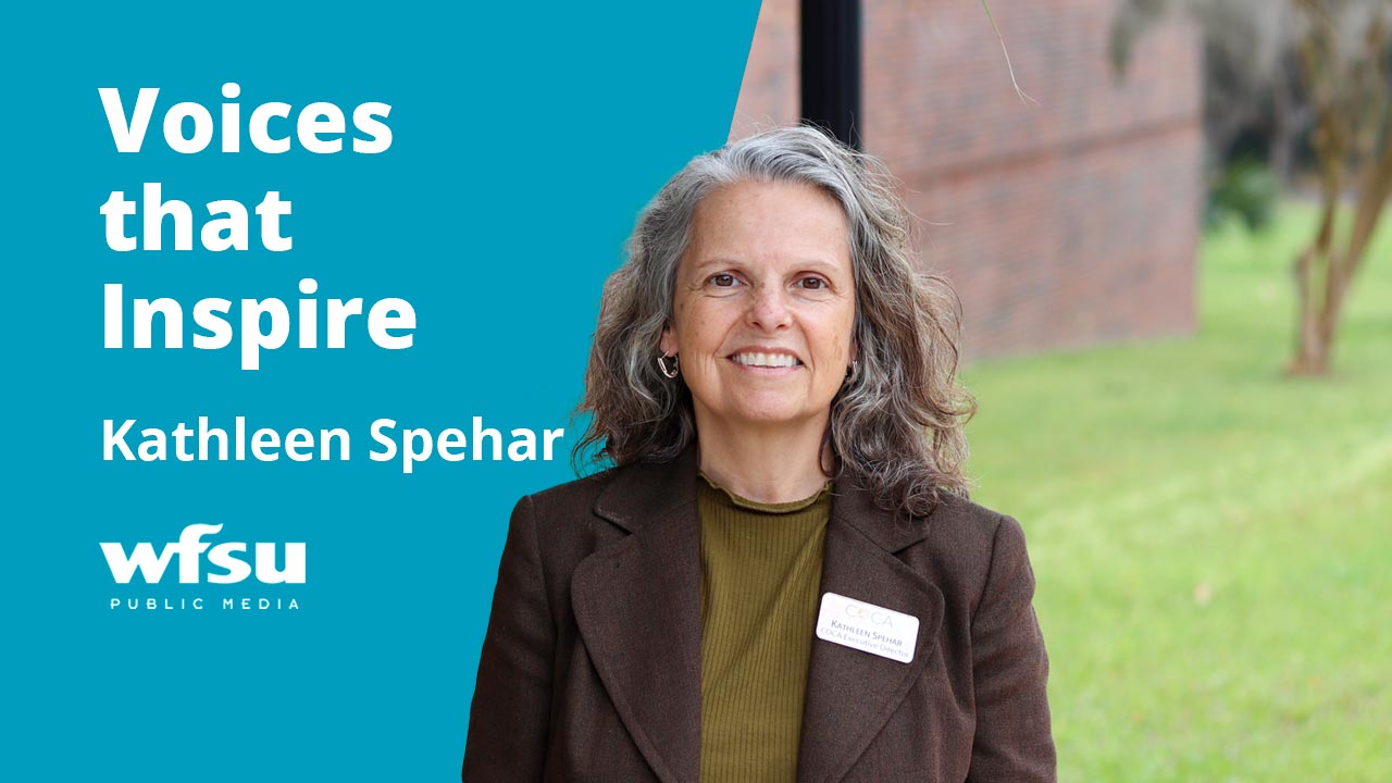A smiling woman stands in front of shrubbery.