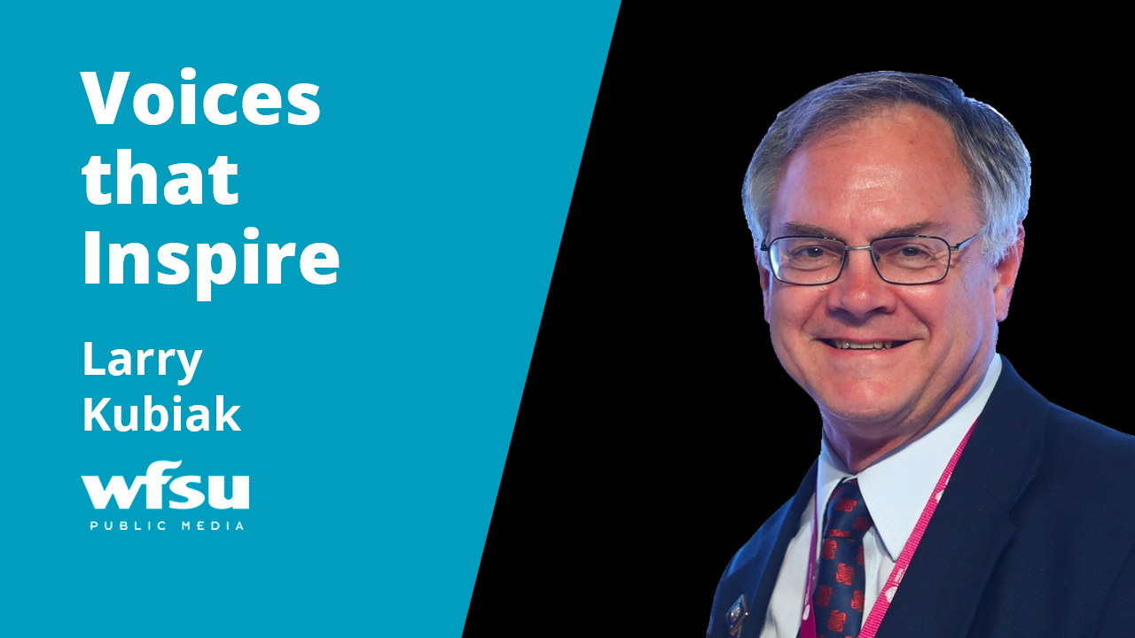 A smiling man in a suit stands outside.