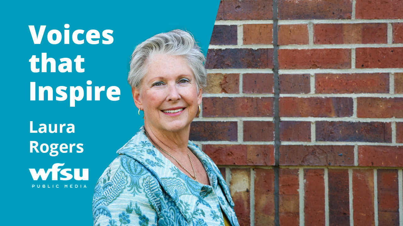 A smiling woman stands in front of a red brick wall.
