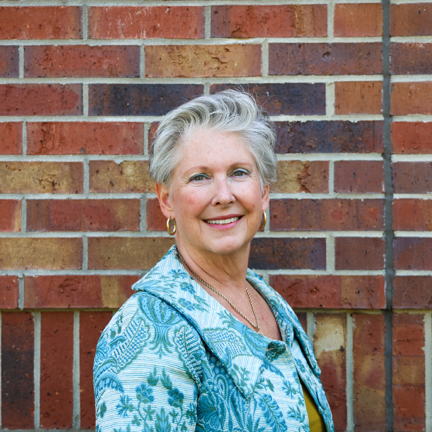 A smiling woman stands in front of a red brick wall.