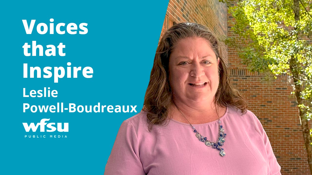 A smiling woman stands in front of a red-brick wall.