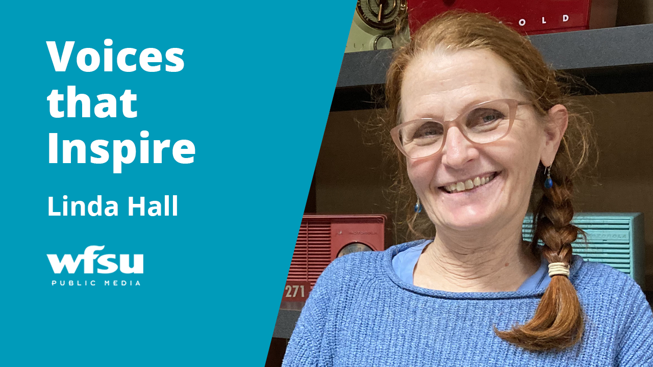 A smiling woman stand in front of a shelf of radios.