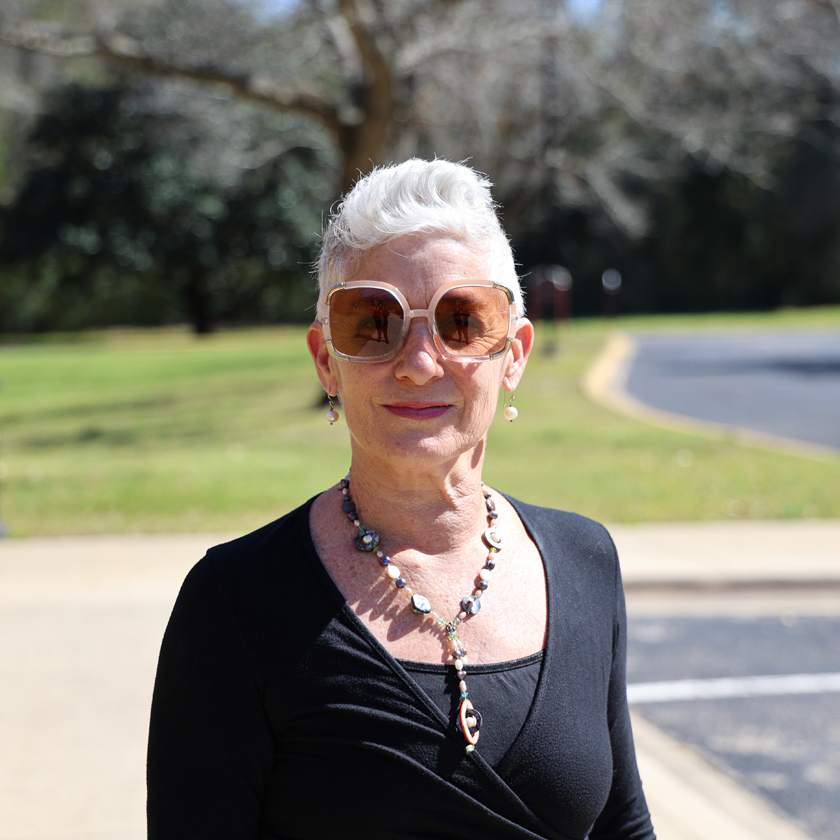 A smiling woman in sunglasses stands outside.