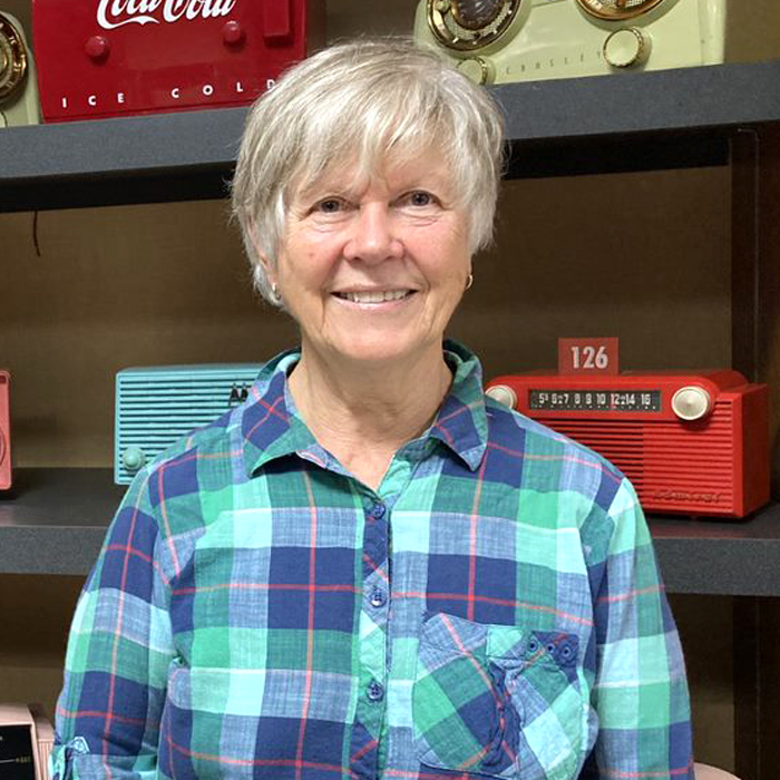 Smiling woman stands in front of a shelf with radios.