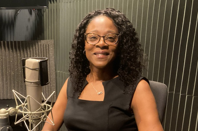 A smiling woman dressed in black sits at a table in front of a microphone. 