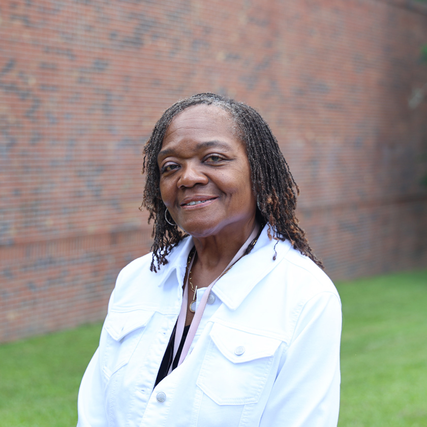 A smiling woman stands in front of a red brick wall.