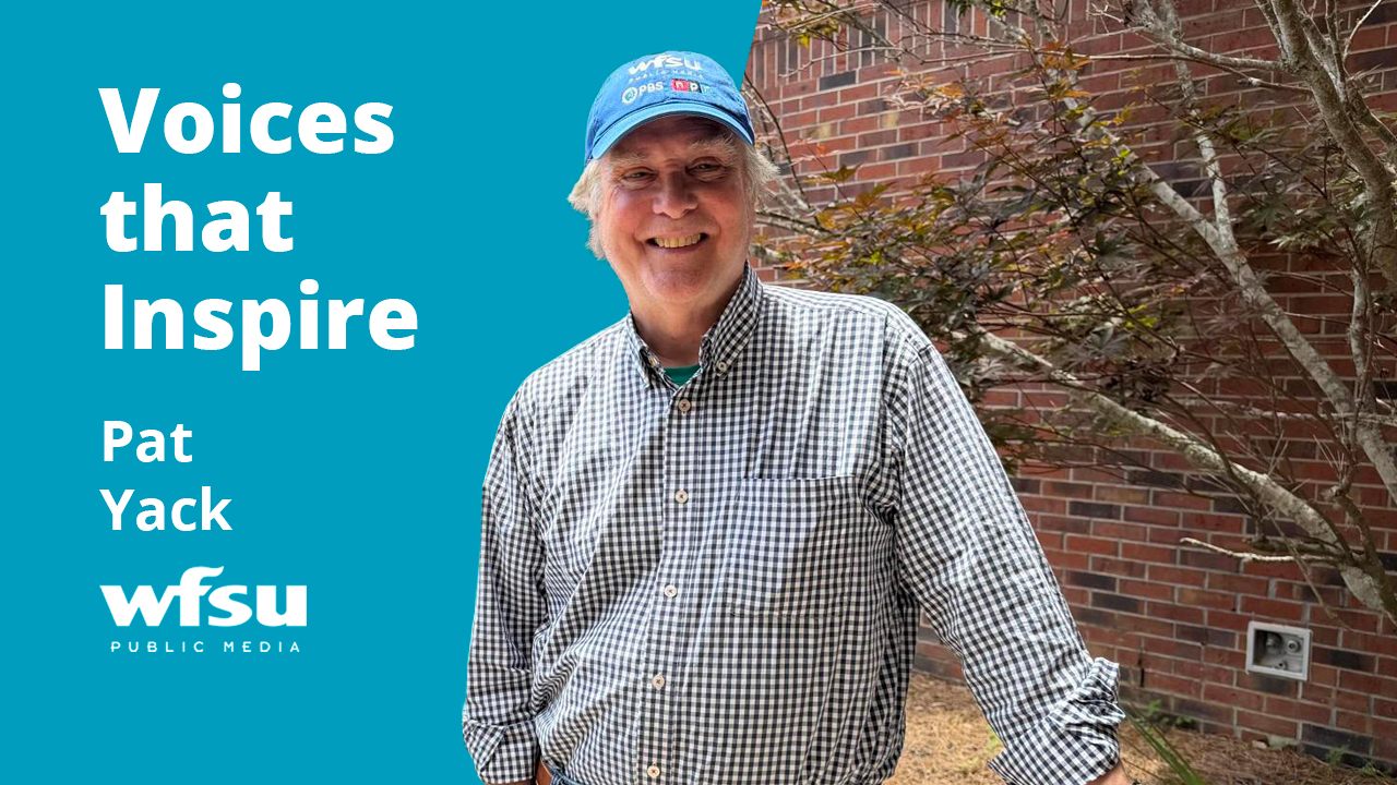 A smiling man in a blue baseball cap stands in front of a red brick wall.