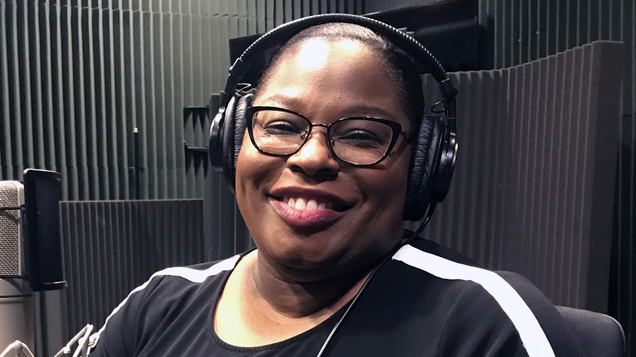 woman in sound-proofed room smiling wearing headphones and glasses