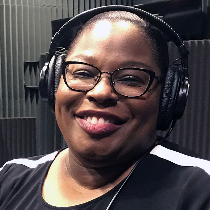 woman in sound-proofed room smiling wearing headphones and glasses