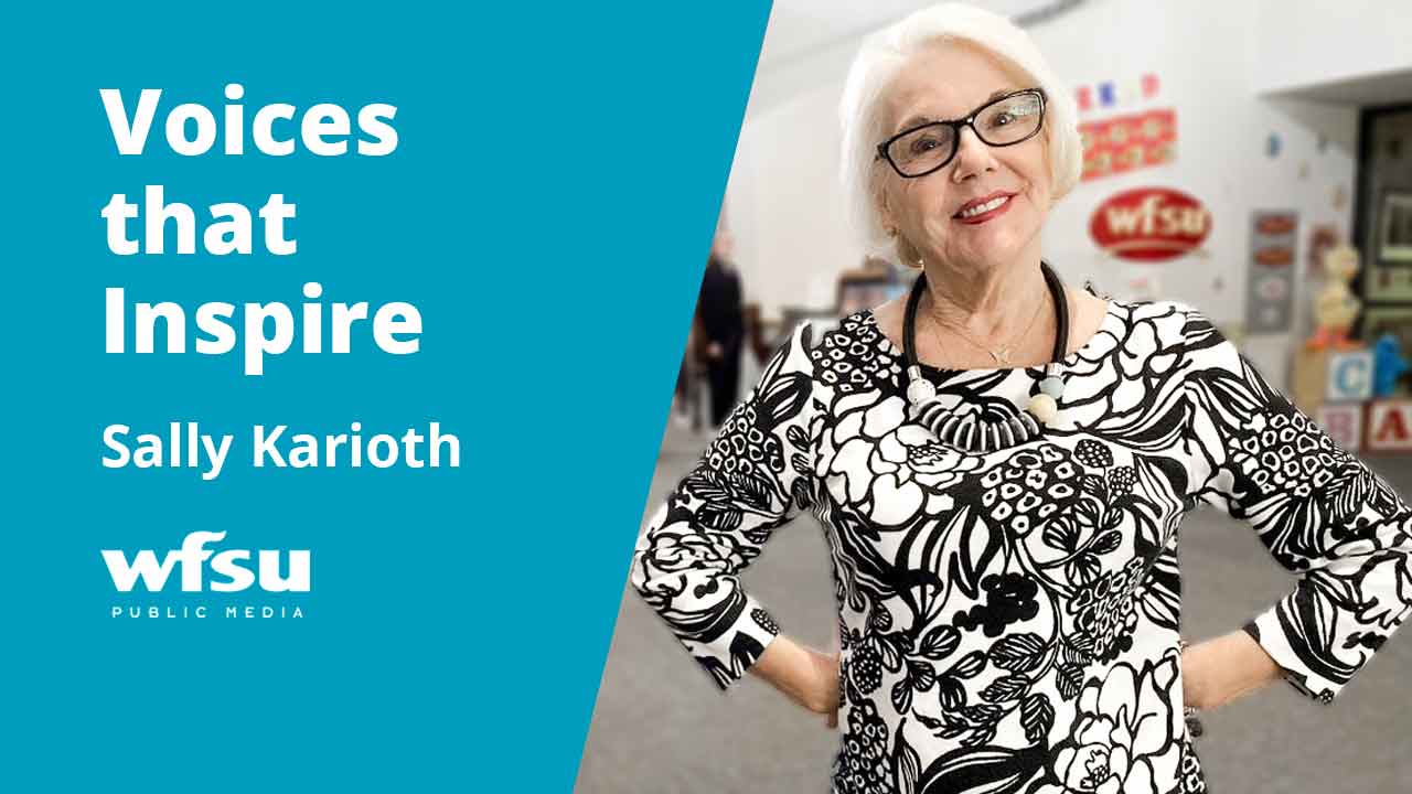 A smiling woman in a white and black dress stands.