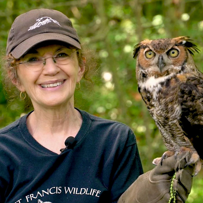 Smiling woman in a hat holds an owl.
