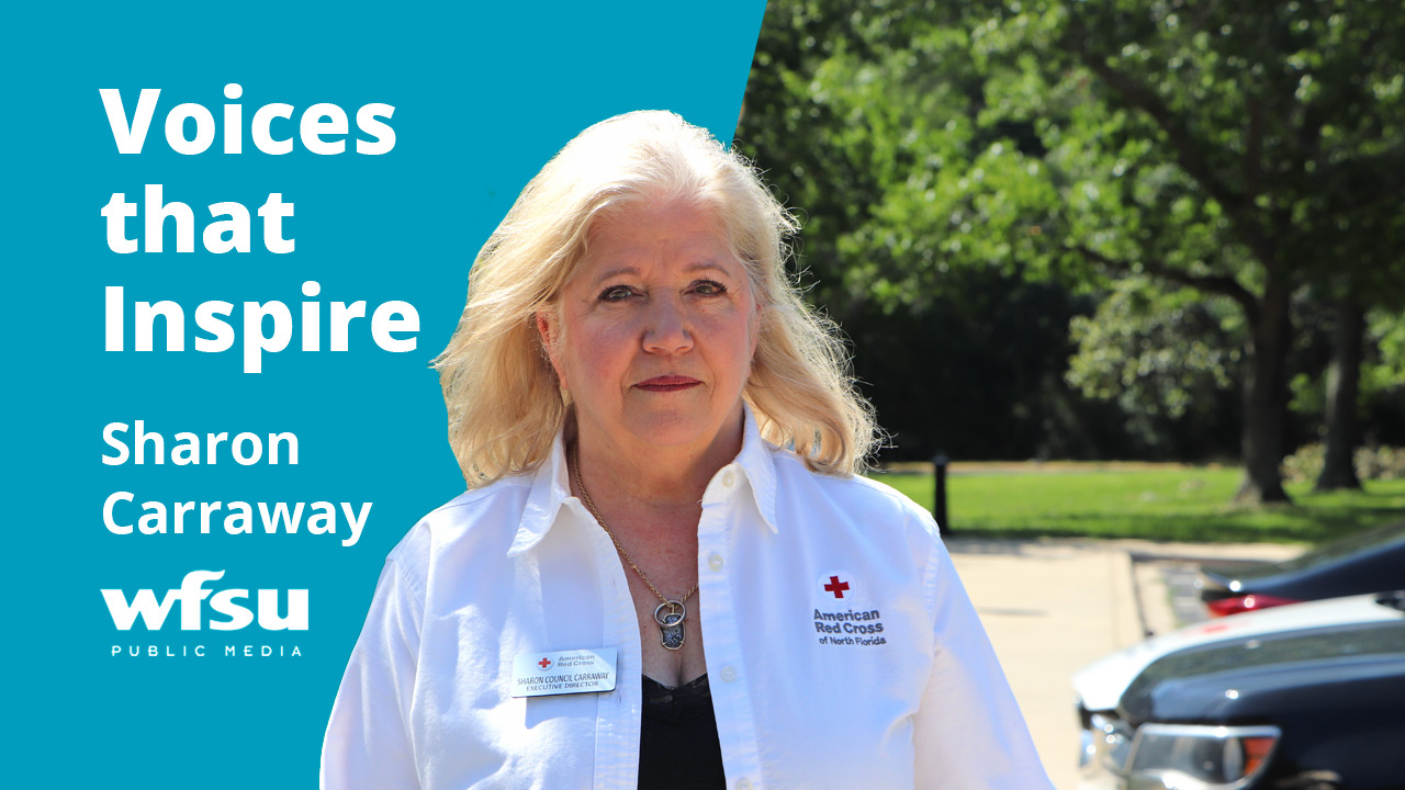 A woman in a white shirt stands outside in front of shrubbery.