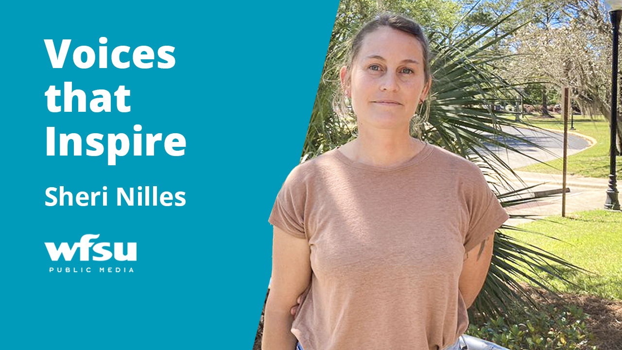 A smiling woman stands in front of green shrubbery. 