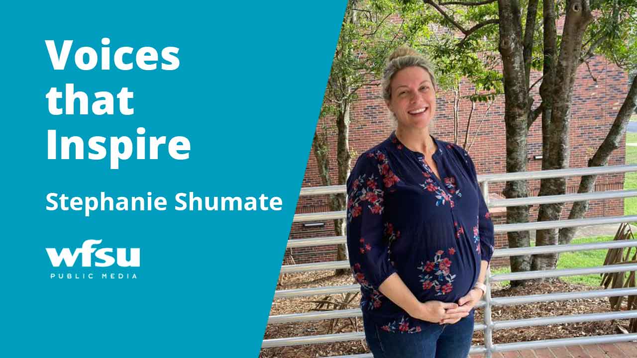 A smiling woman stands in front of shrubbery.