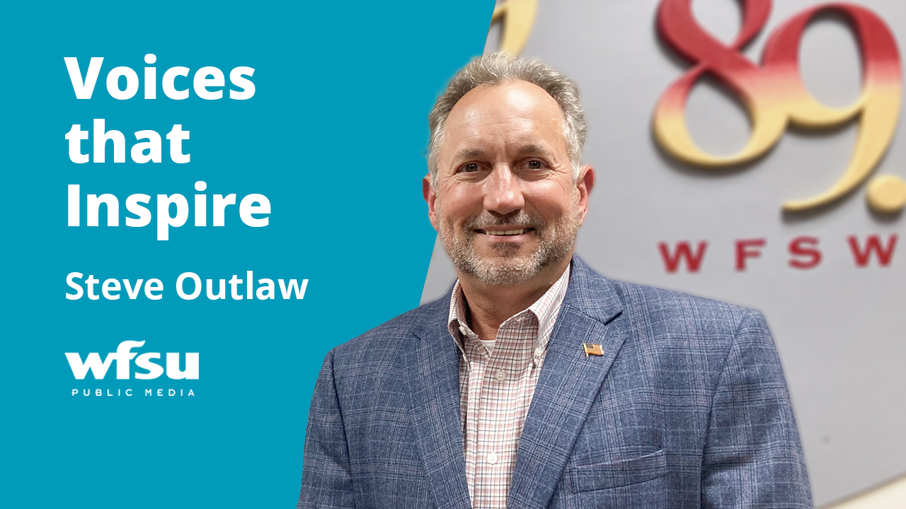 A smiling man in a blue suitcoat stares forward smiling.