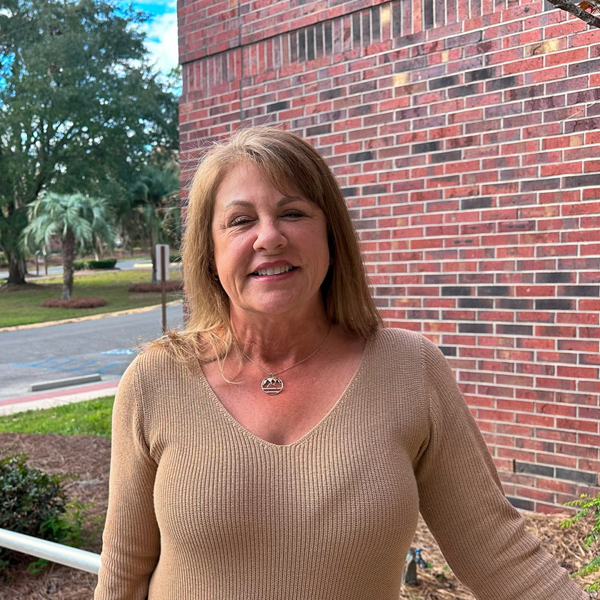 A smiling woman stands outside in front of a red brick wall.