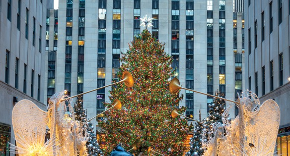 Light decorated christmas tree pictured in time square with angel statues playing trumpets