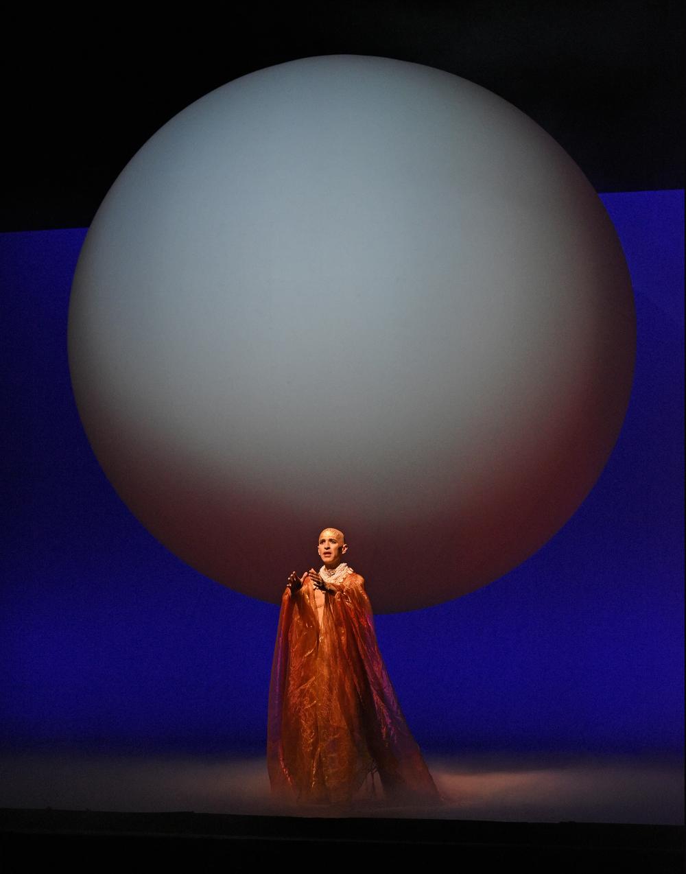 Person in red performing infront of a globular structure