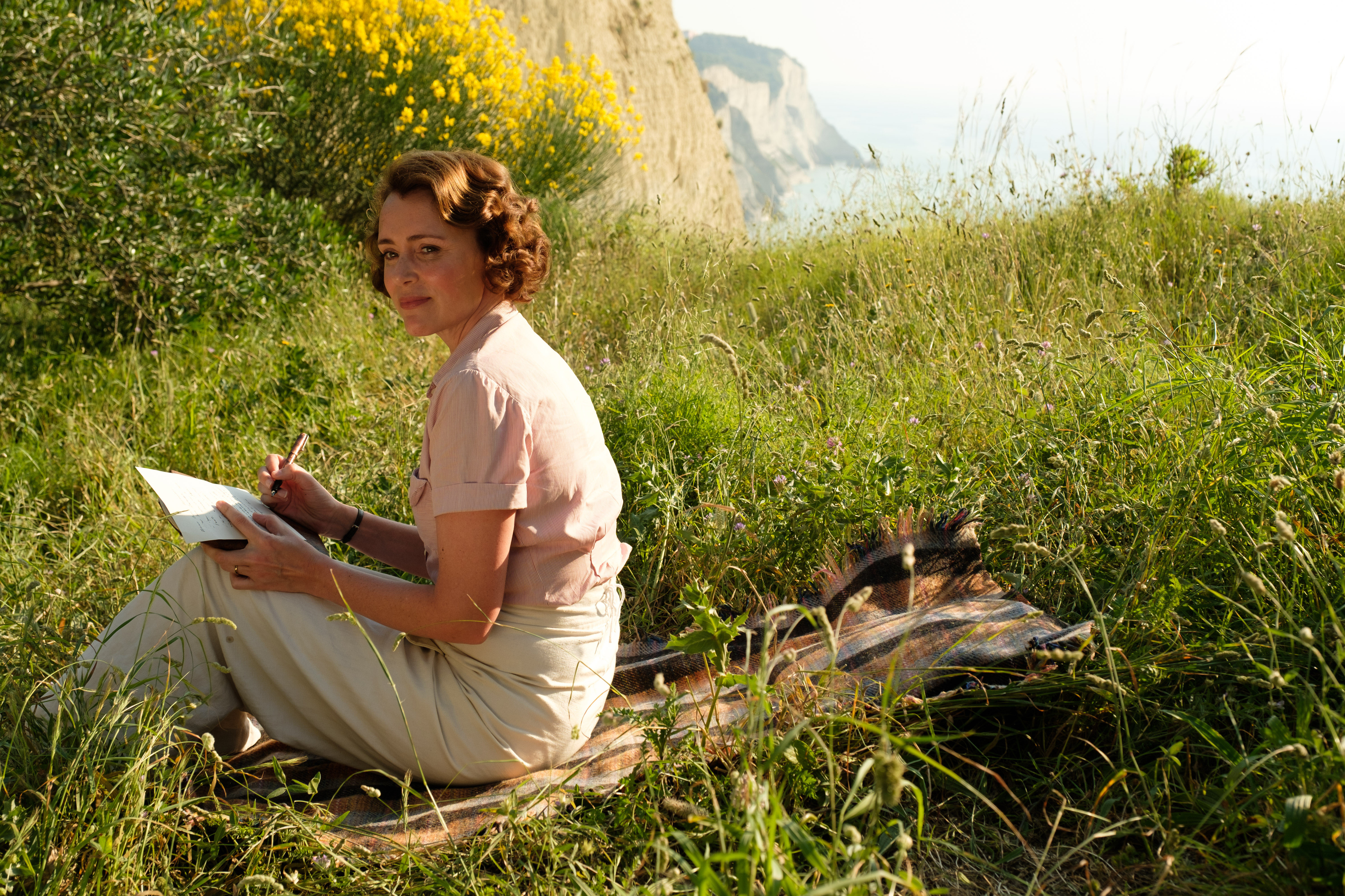 girl in a field with cliff in the background, writing