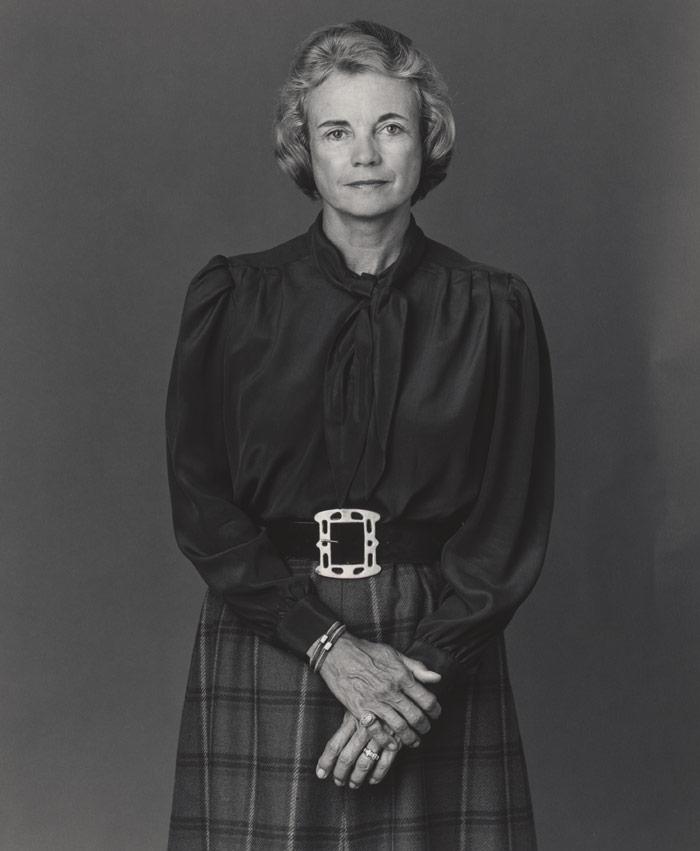 black and white photo of woman in smart skirt and long-sleeved shirt looking into camera