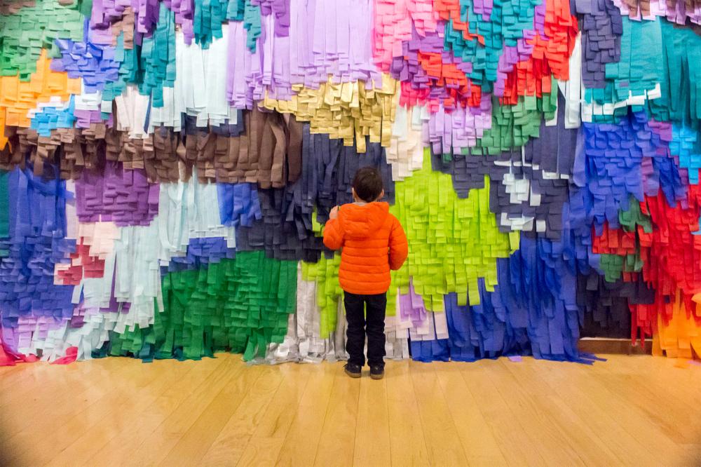 Child standing in front of a colored art wall.