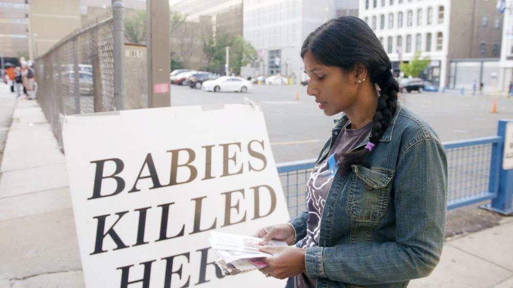 Women standing sadly in front of an anti-abortion sign.