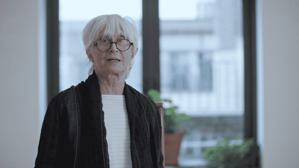 twyla tharp, white straight hair and round black glasses in a black jacket and white shirt