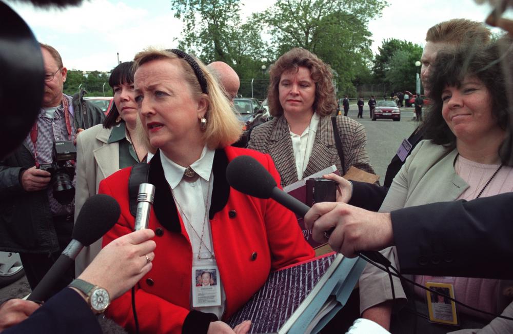 Distraught woman being uncomfortably surrounded by reporters with giant microphones