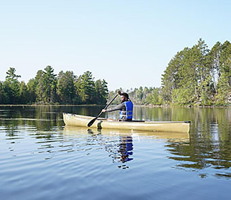 man paddling in canoe on body of water with trees in background